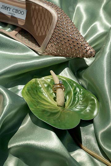 Mit Schmucksteinen besetzter Brautschuh neben einem grünen Accessoire auf Satin.