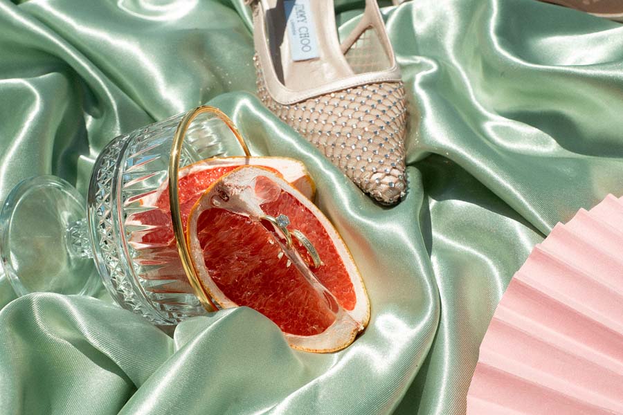 Brautschuh, Grapefruithälfte, rosafarbener Fächer und Accessoires auf grünem Satin.