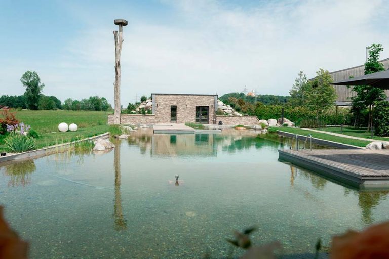 See mit begrünten Ufern, Wegen und einem Pavillon im Hintergrund.