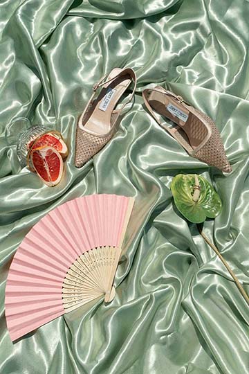 Brautschuhe, rosafarbener Fächer und kleine Accessoires auf grünem Satin.