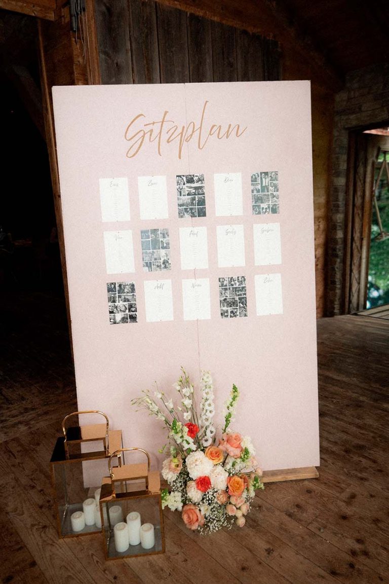 Heller Sitzplan auf einer Staffelei mit weißen und orangefarbenen Blumen vor einer Holzwand.