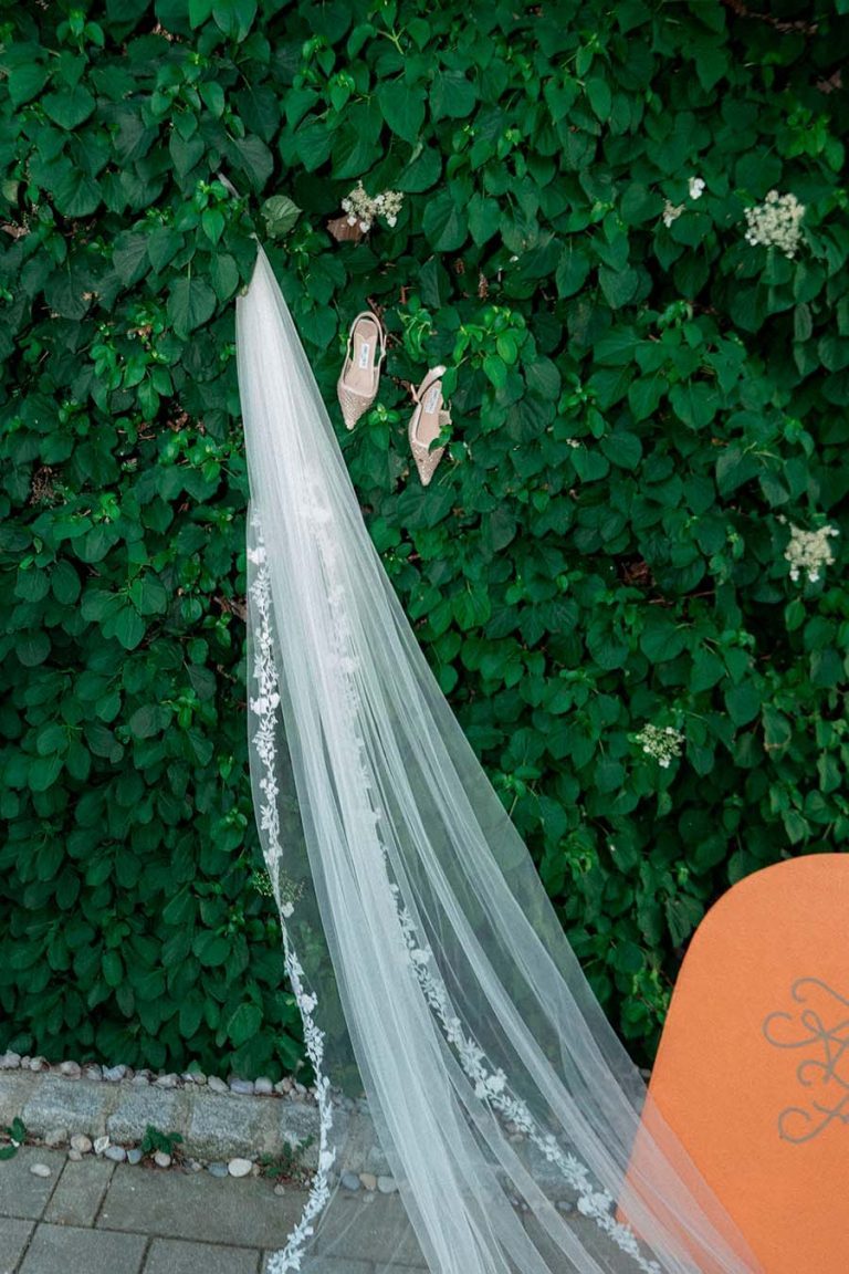 Weißer Brautschleier vor einer begrünten Holzwand neben einem orangefarbenen Dekoelement.