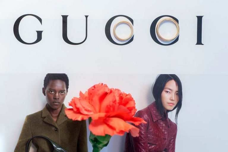 Orangefarbene Blüte vor einem aufgeschlagenen Gucci-Motiv mit zwei Models.