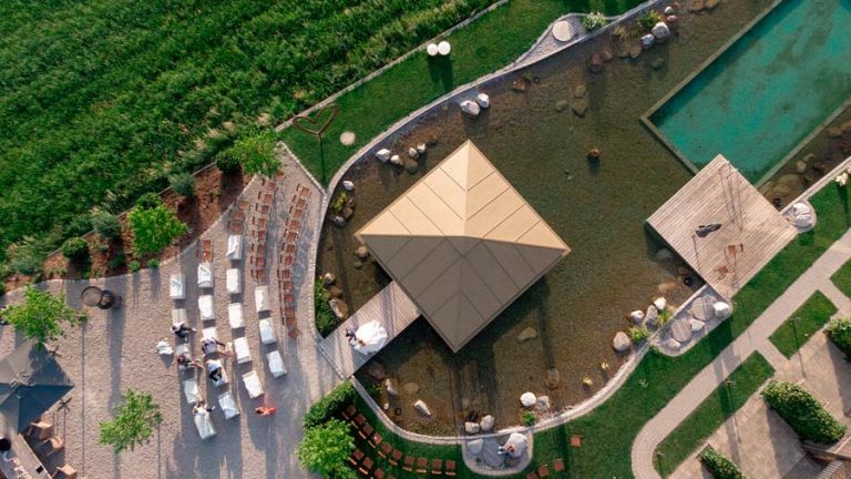 Luftaufnahme eines Holzpavillons am Wasser mit umliegenden Wegen und Grünflächen.
