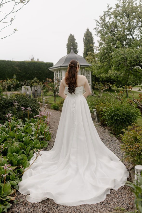 Braut im wunderschönen weißen Kleid betritt den romantischen Garten der Location Fitz-Ritter