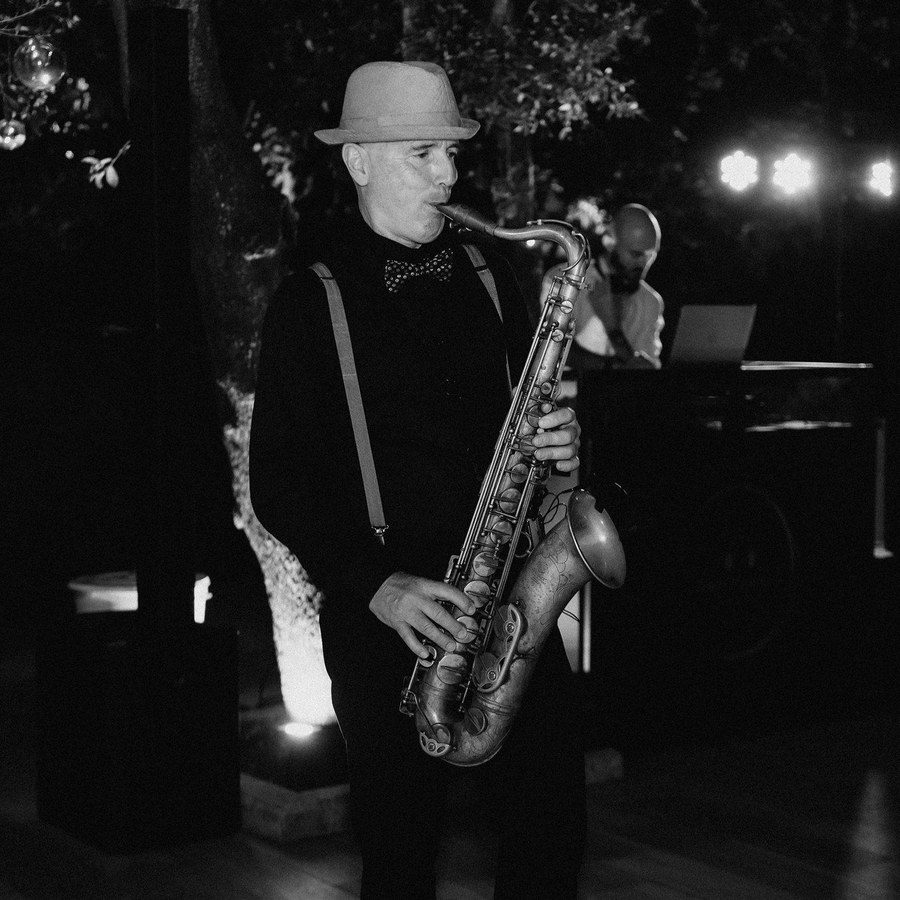 Eventplanung Italien: Saxophonist mit Hut spielt abends neben dem DJ-Pult, Schwarz-Weiß-Aufnahme
