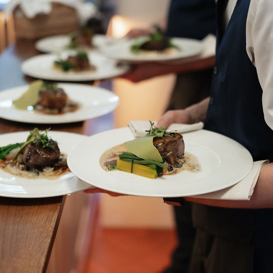 Eventplanung Starnberg: Servicekraft trägt angerichtete Teller zum Hochzeitsdinner