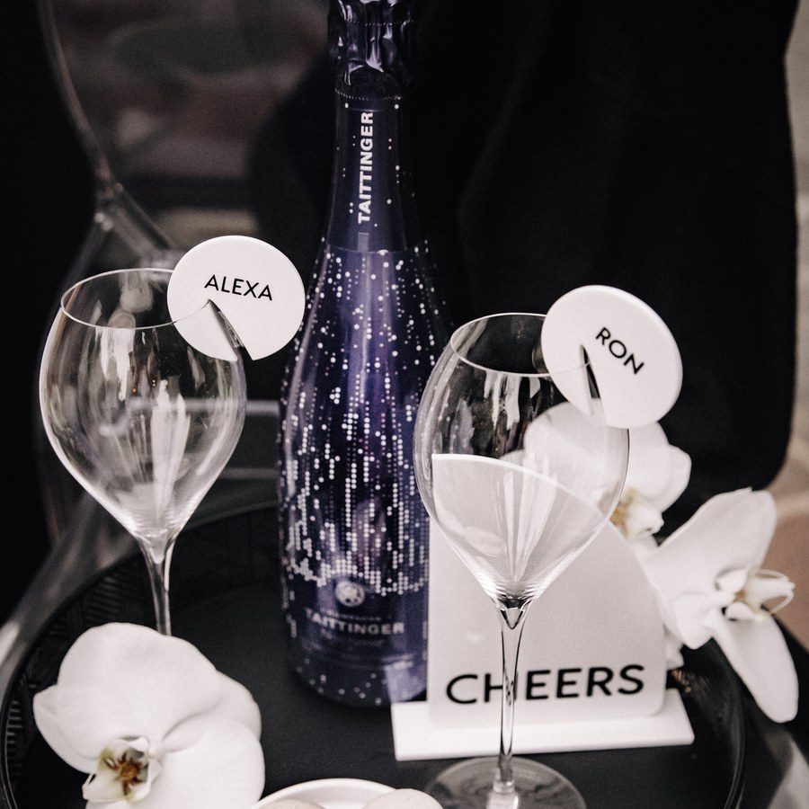 Eventplanung Südtirol: Champagnerflasche, Gläser mit Namensschildern, Macarons und Orchideen auf dem Beistelltisch