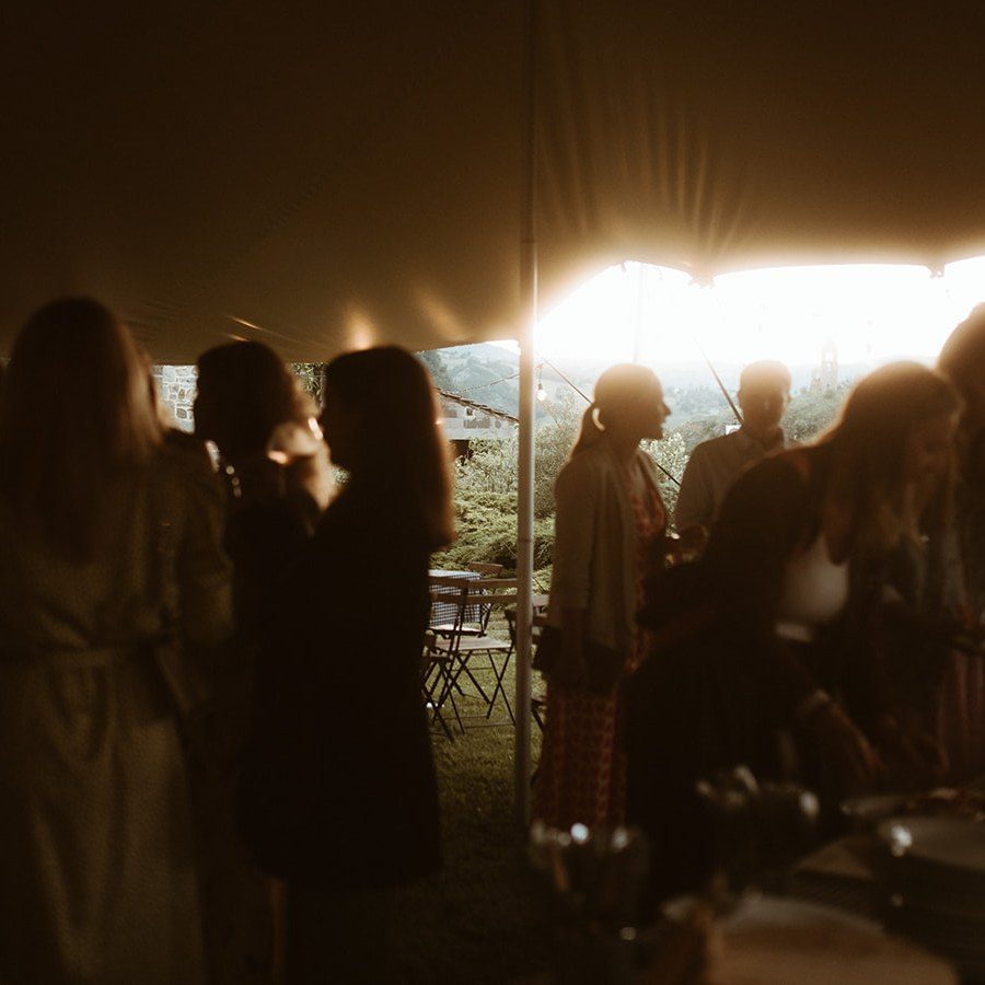 Eventplanung Toskana: Gäste stehen abends unter einem Zeltdach beim Pizzaabend im warmen Lichterschein
