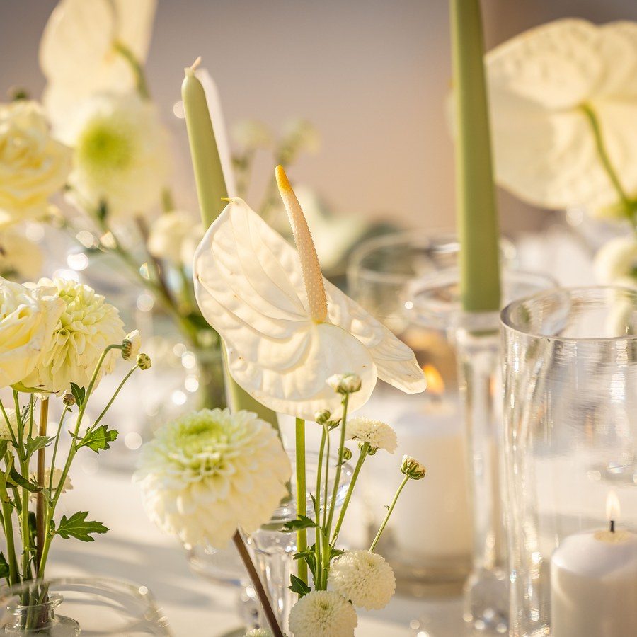 Eventplanung Verona: weißes Blumenarrangement aus Rosen, Dahlien und Anthurien zwischen Kerzen auf der Tafel