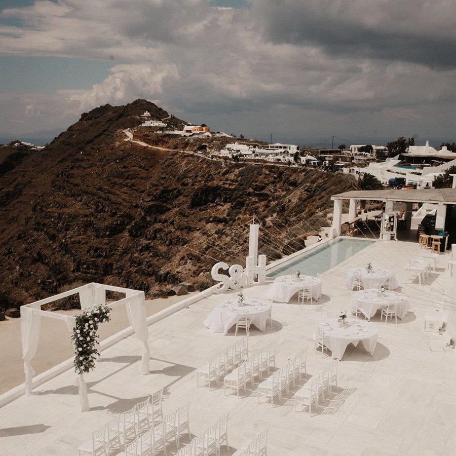 Freie Trauung Santorini: weiße Stuhlreihen und Traubogen auf der Terrasse am Pool vor der Vulkanlandschaft
