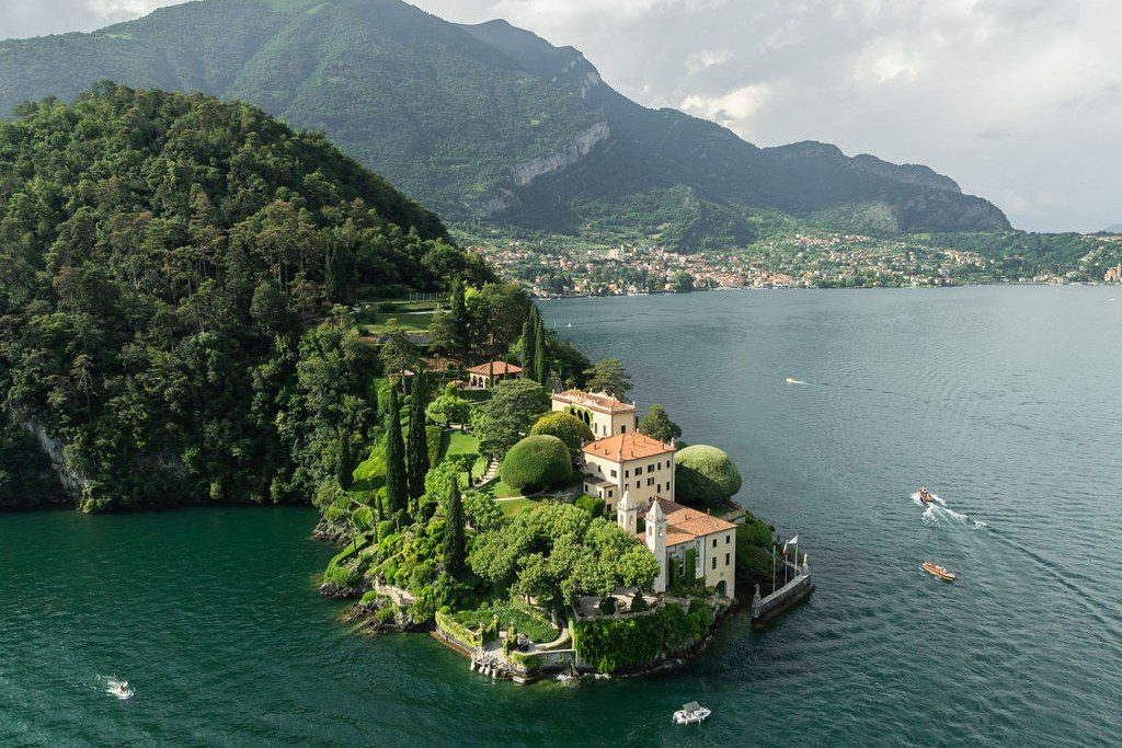 Luftbild einer Villa mit Terrassengärten auf einer bewaldeten Halbinsel im Comer See