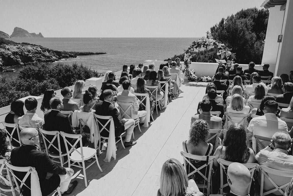Hochzeitsgesellschaft sitzt bei der Zeremonie auf der Terrasse über der Bucht, Schwarz-Weiß-Aufnahme