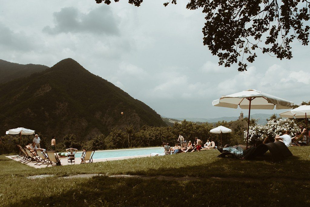 Pool eines toskanischen Landguts mit Sonnenschirmen, dahinter bewaldete Hügel im Abendlicht