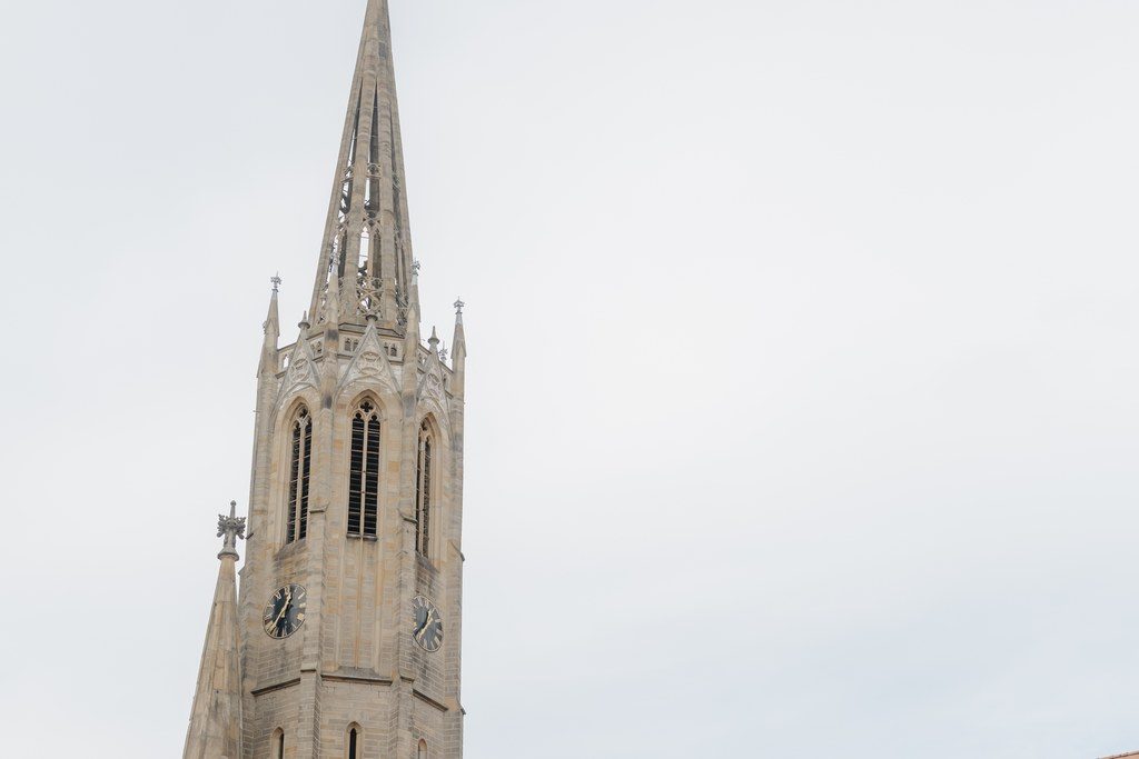 Gotische Kirche mit hohem Turm am Marktplatz einer pfälzischen Weinstadt vor bewaldeten Hügeln