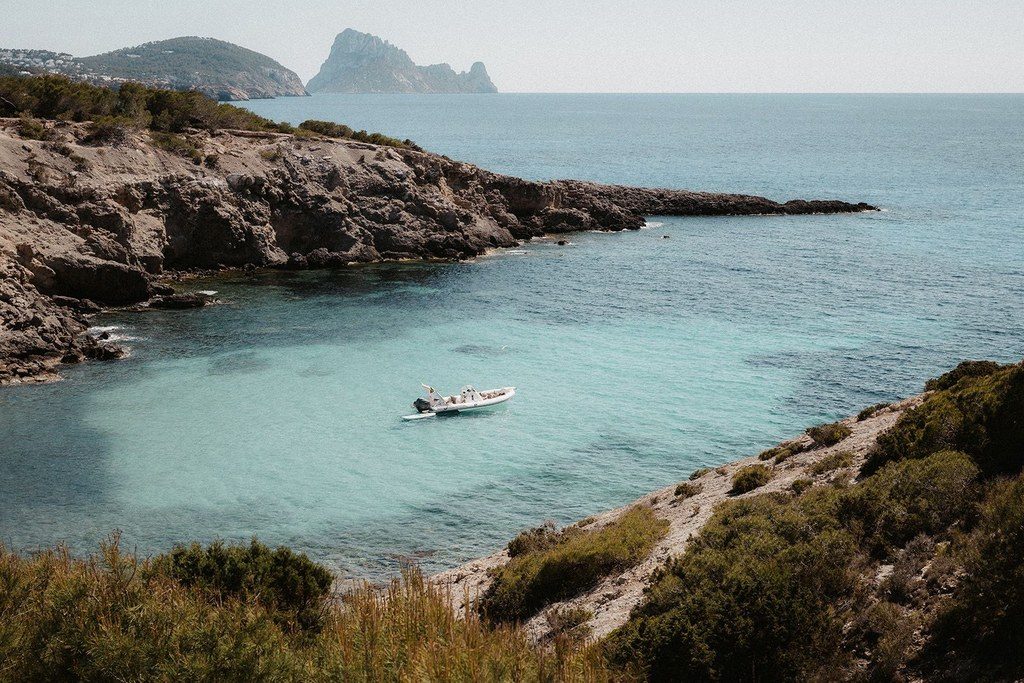 Türkisfarbene Bucht mit einem einzelnen Boot, im Hintergrund die vorgelagerte Felseninsel
