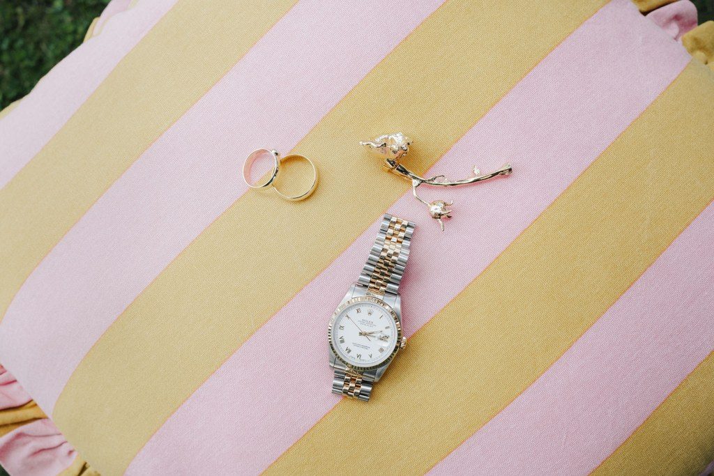 Eheringe, Kette und Armbanduhr liegen auf einem rosa-gelb gestreiften Kissen