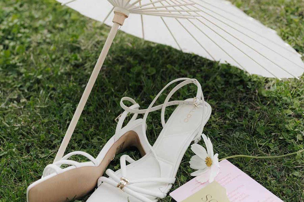 Brautschuhe, Papierschirm und Papeterie liegen auf der sommerlichen Wiese vor der Trauung