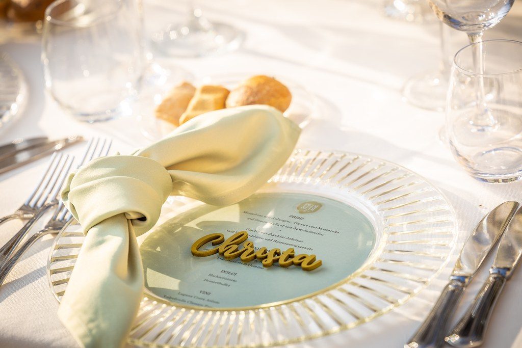 Gedeck mit geknoteter Serviette, Menükarte und goldenem Namensschild auf dem Glasteller