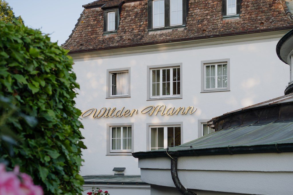 Efeubewachsenes historisches Gasthaus am Hang über dem Bodensee, davor blühende Rosen