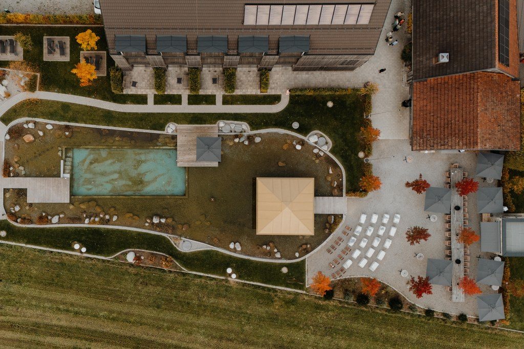 Luftbild einer Hochzeitslocation mit Naturteich, Pavillon und weißen Stuhlreihen im Herbst