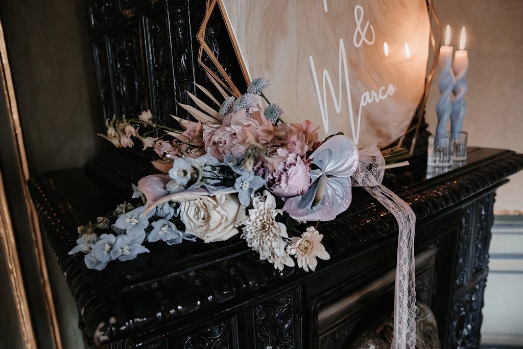 Hochzeitsplaner Stuttgart: schwarzer Kaminsims mit Blumenlauf in Flieder und Rosé, Kerzen und Namensschild des Brautpaars