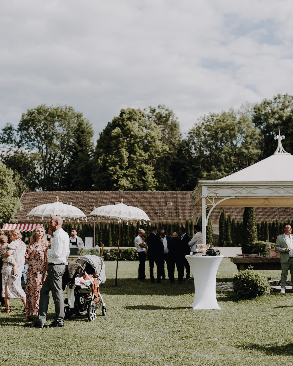 Hochzeitsplanerin Baden-Württemberg: Gäste beim Sektempfang im Park, im Hintergrund ein weißer Pavillon