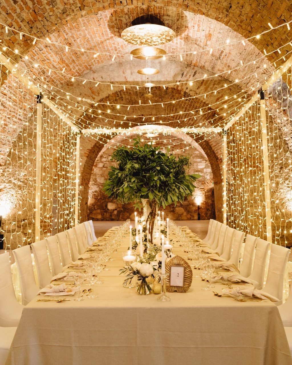 Hochzeitsplanerin Bayern: lange weiße Tafel in einem Gewölbe, dessen Wände vollständig mit Lichterketten bespannt sind
