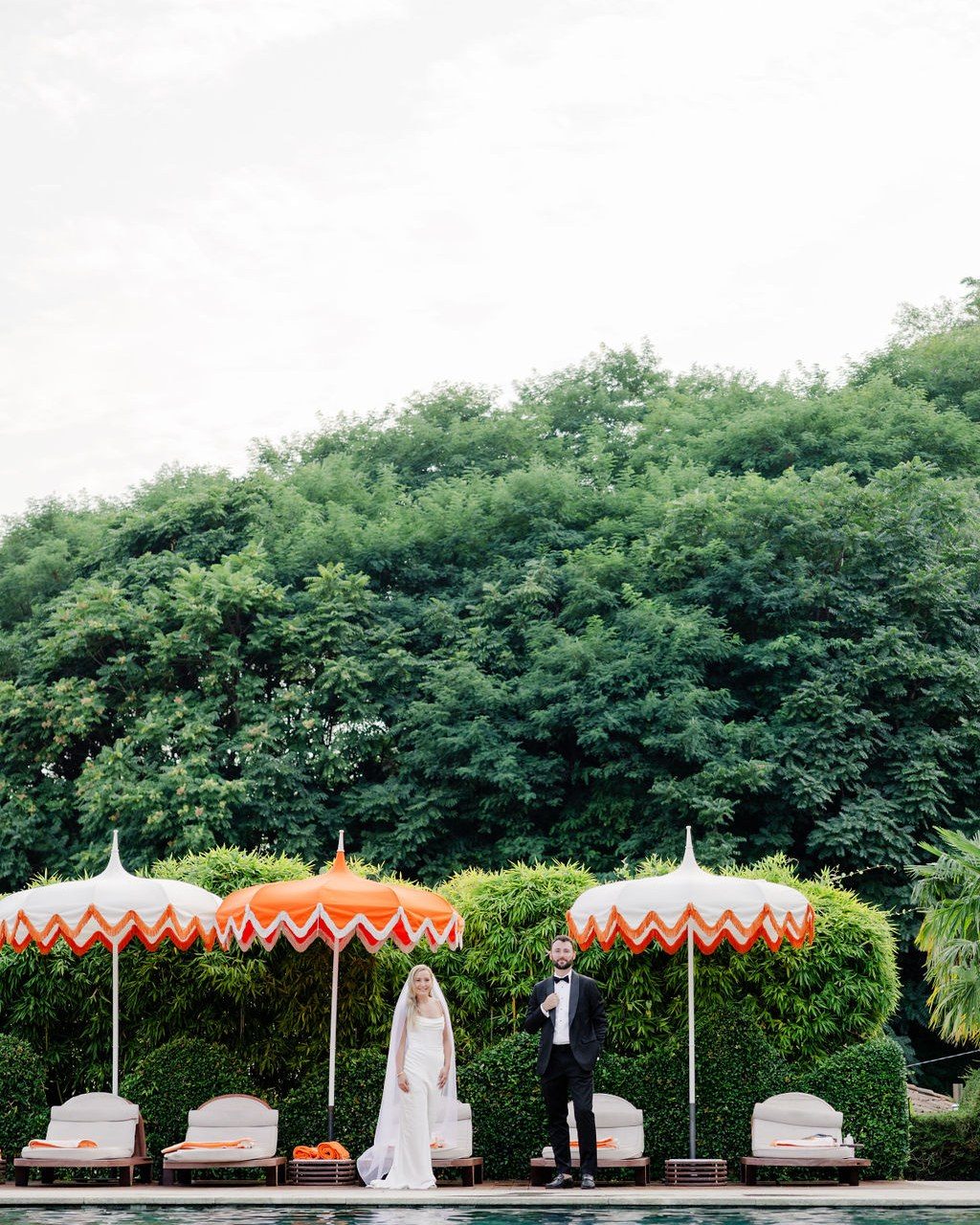 Hochzeitsplanerin Comer See: Brautpaar steht zwischen orange gestreiften Sonnenschirmen an der Poolterrasse