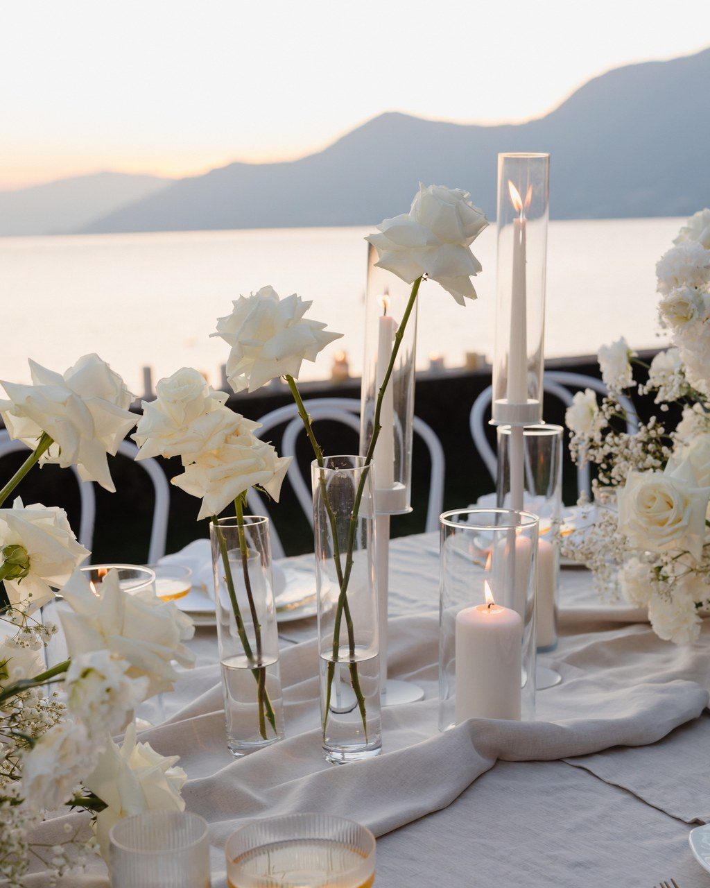 Hochzeitsplanerin Lago Maggiore: Tischdekoration mit weißen Blüten und Stabkerzen vor dem Seeblick im Abendlicht