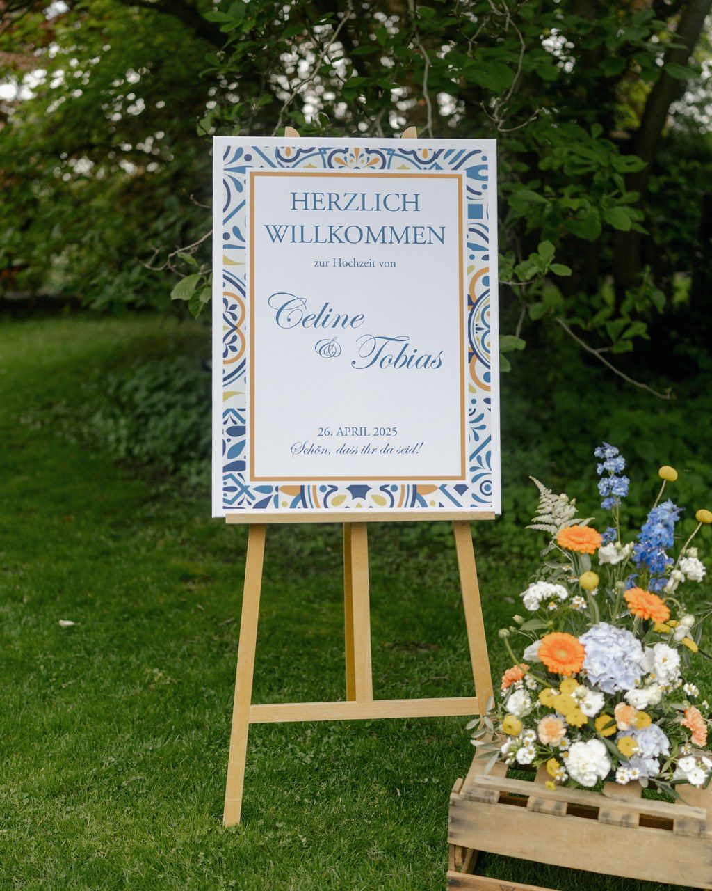 Hochzeitsplanerin Rheinland-Pfalz: blau-weißes Willkommensschild des Brautpaars auf der Staffelei, umrahmt von Sommerblumen