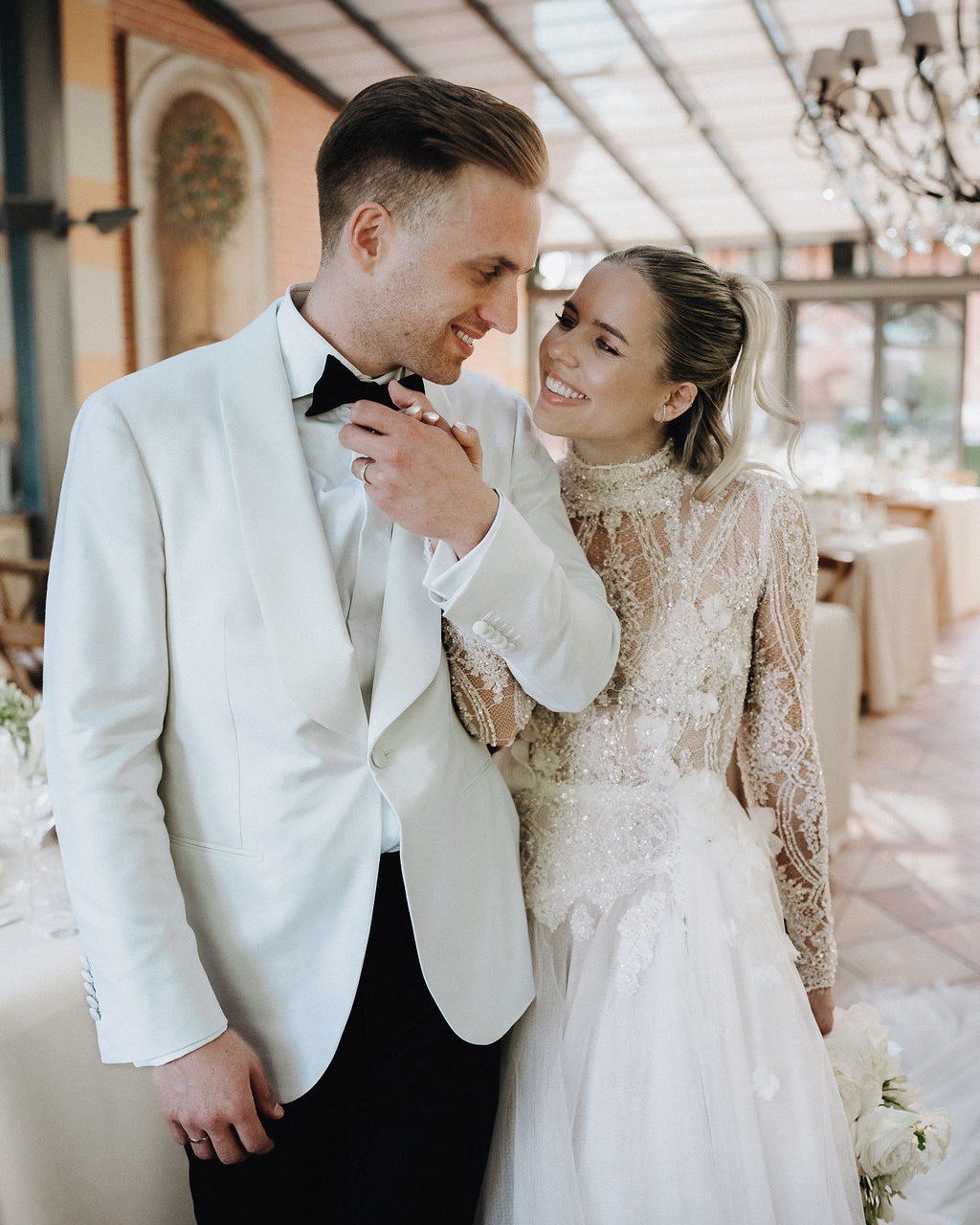 Hochzeitsplanerin Starnberg: Brautpaar lacht sich im Wintergarten an, er im weißen Dinnerjacket, sie im Spitzenkleid