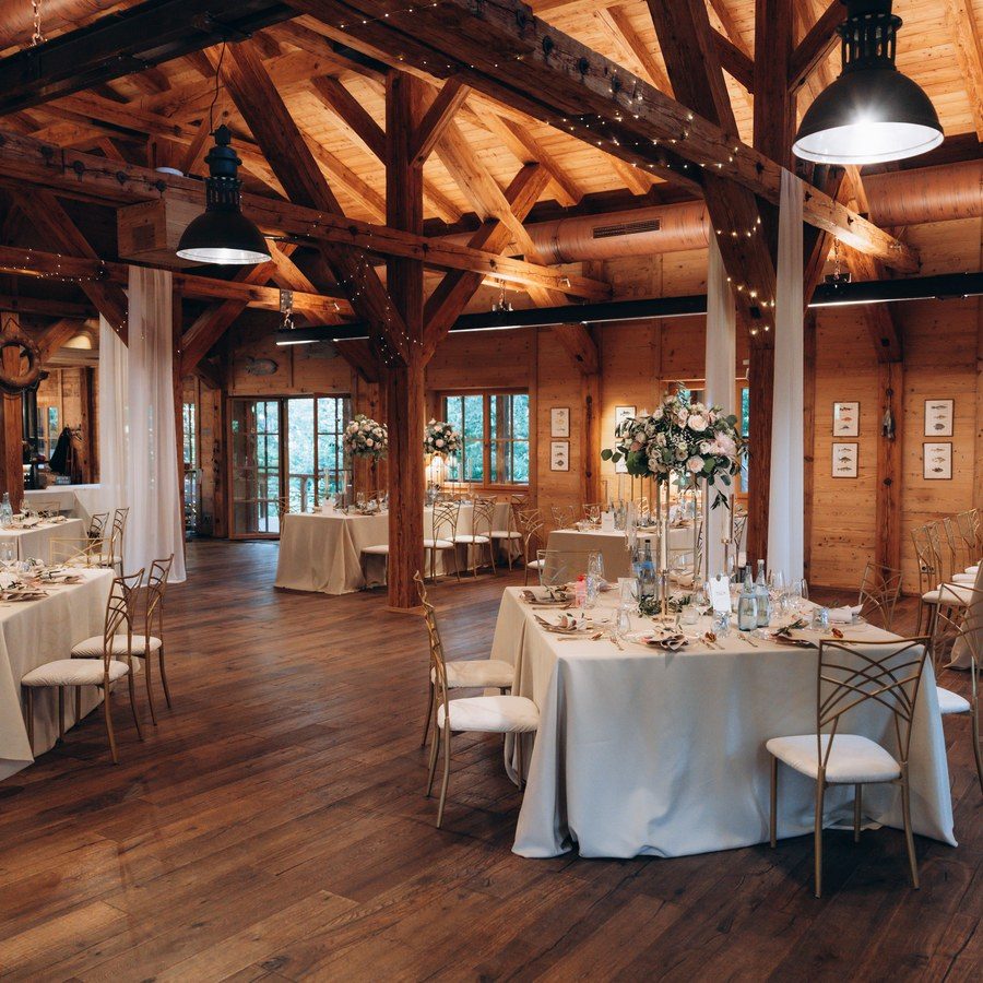Hochzeitsplanung Allgäu: eingedeckte runde Tafeln unter alten Holzbalken und Lichterketten in einem Stadel