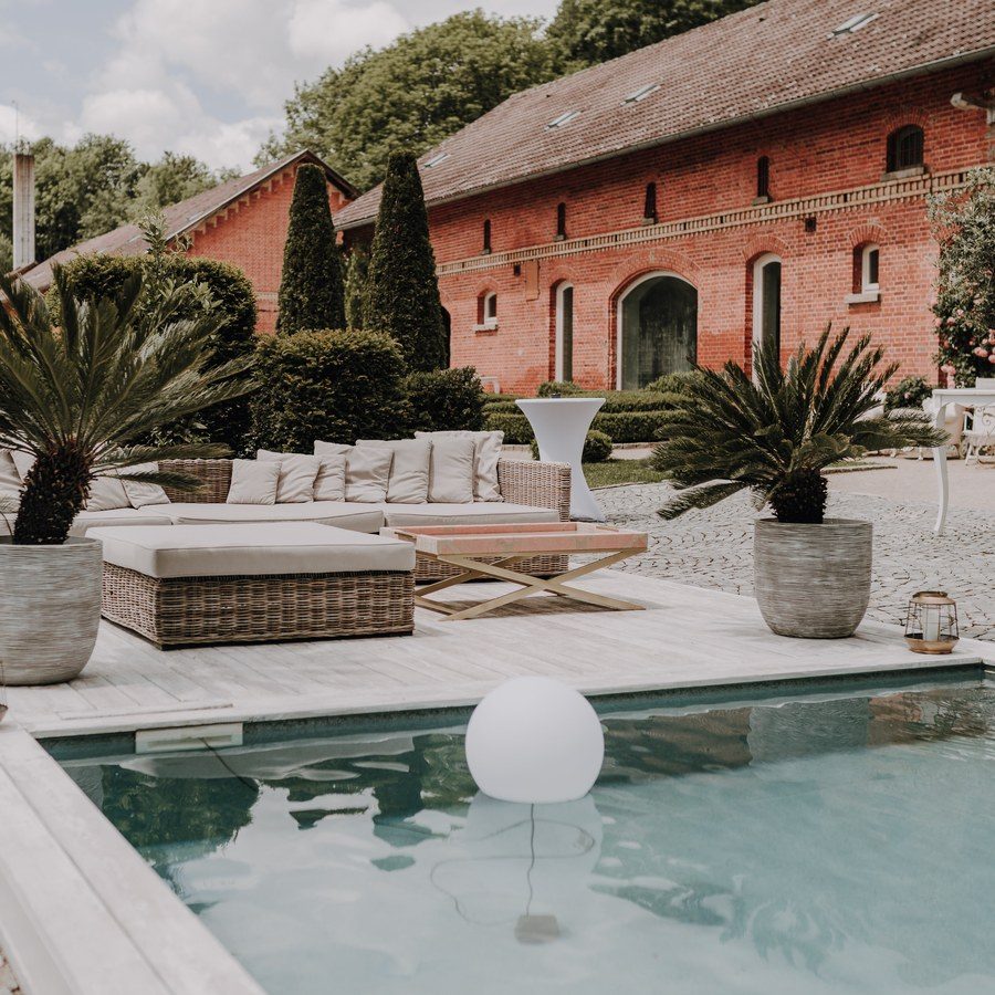 Hochzeitsplanung Baden-Württemberg: Backsteingut mit Pool, Lounge-Möbeln und Palmen als sommerliche Hochzeitslocation