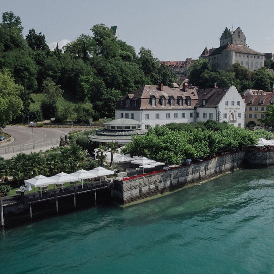 Hochzeitsplanung Bodensee: Luftbild der Uferpromenade mit Hotel, Anlegestelle und Burg über dem türkisfarbenen Wasser
