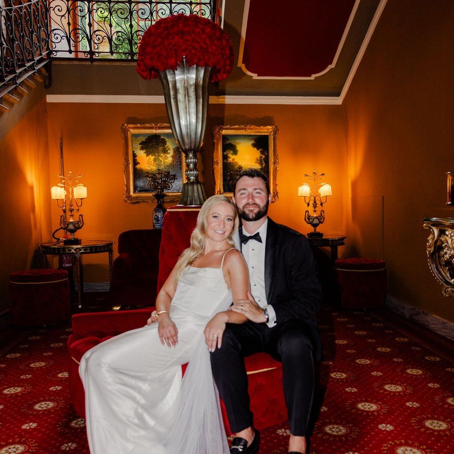 Hochzeitsplanung Frankfurt: Brautpaar auf einem roten Samtsofa in einem historischen Salon mit Kronleuchter-Licht
