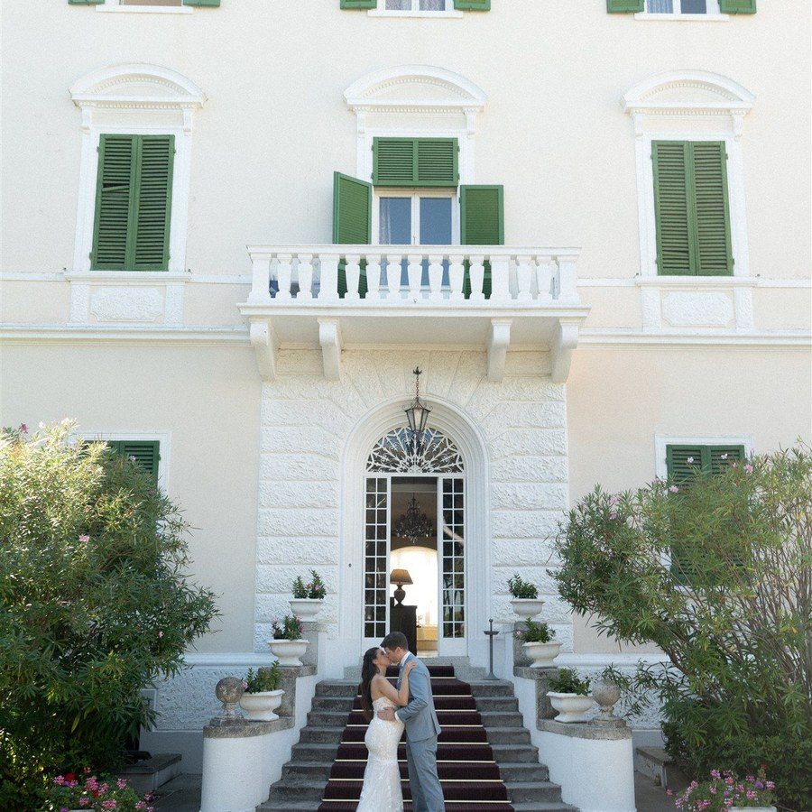 Hochzeitsplanung Italien: Brautpaar steht auf der Freitreppe einer Villa mit grünen Fensterläden