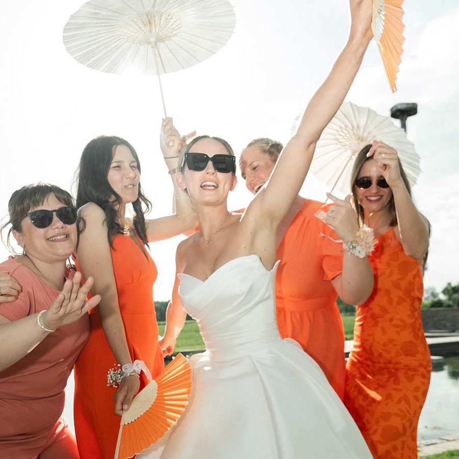 Hochzeitsplanung Mannheim: Braut jubelt mit ihren Trauzeuginnen in Orange, mit Papierschirmen und Fächern
