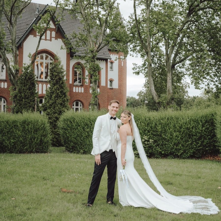 Hochzeitsplanung NRW: Brautpaar vor historischer Backsteinvilla im Grünen