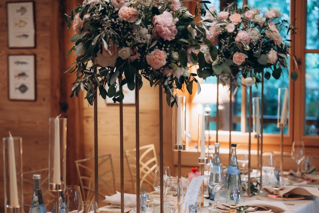Hochzeitstafel im Allgäu mit hohen Blumenarrangements in Rosé, Kerzen und Wasserflaschen im holzverkleideten Saal