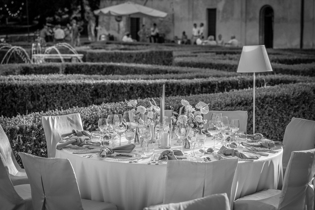 Runde, weiß eingedeckte Hochzeitstafeln zwischen geschnittenen Buchshecken im Garten, Schwarz-Weiß