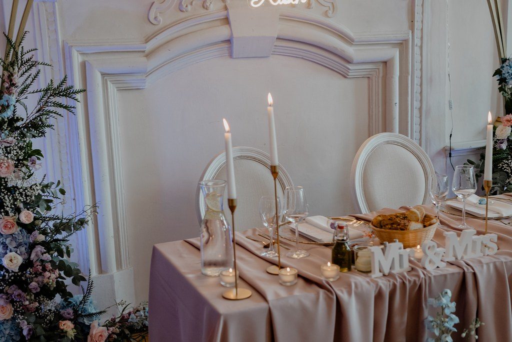 Brauttisch mit Kerzen, Hortensien und Neonschriftzug vor einer Stuckwand im Schlosssaal