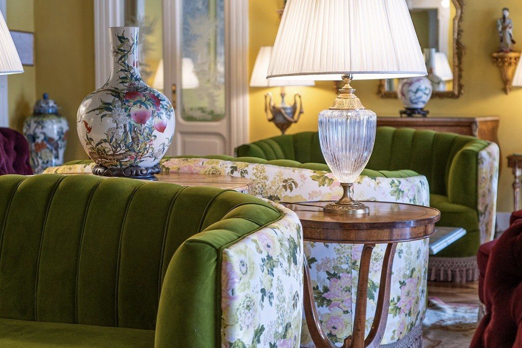 Salon mit grünen Samtsesseln, geblümten Polstern, Porzellanvase und Tischlampe