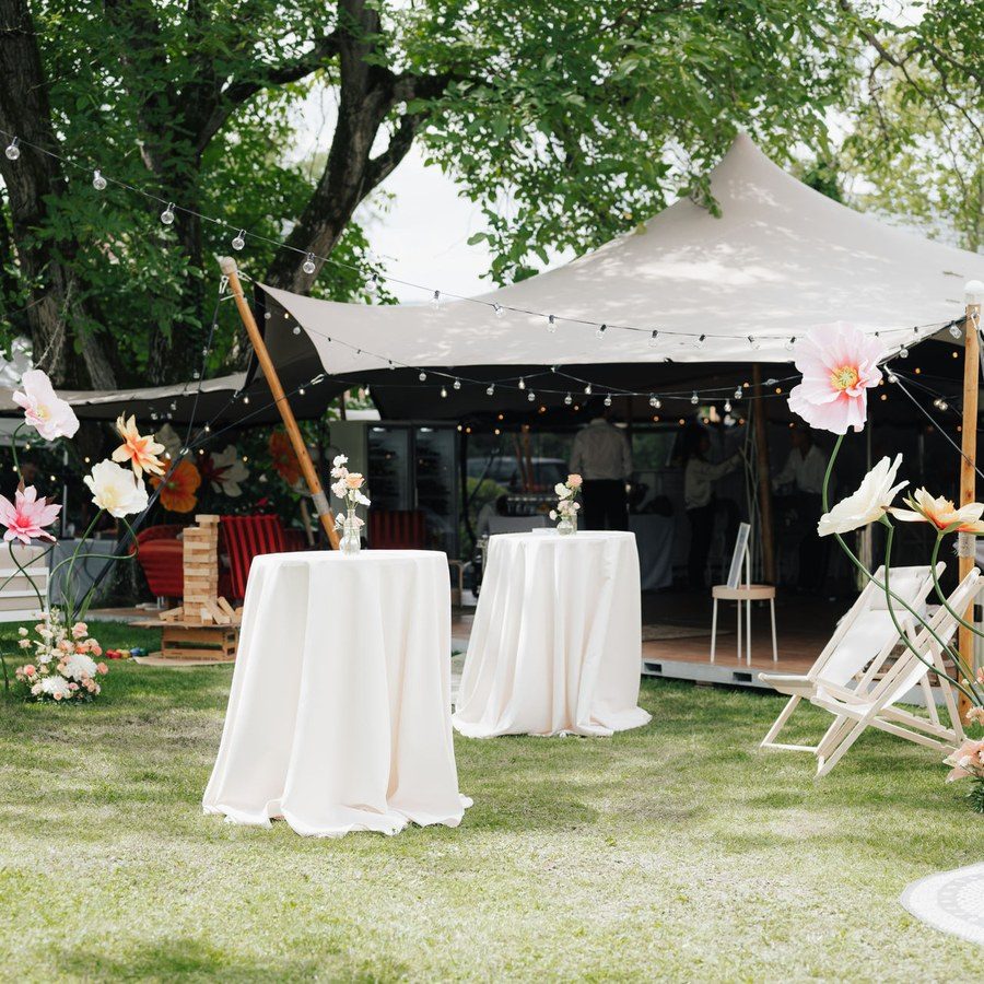 Hochzeitsplanung Zelthochzeit: weißes Gartenzelt mit Lichterketten, Stehtischen und großen Papierblumen im Grünen